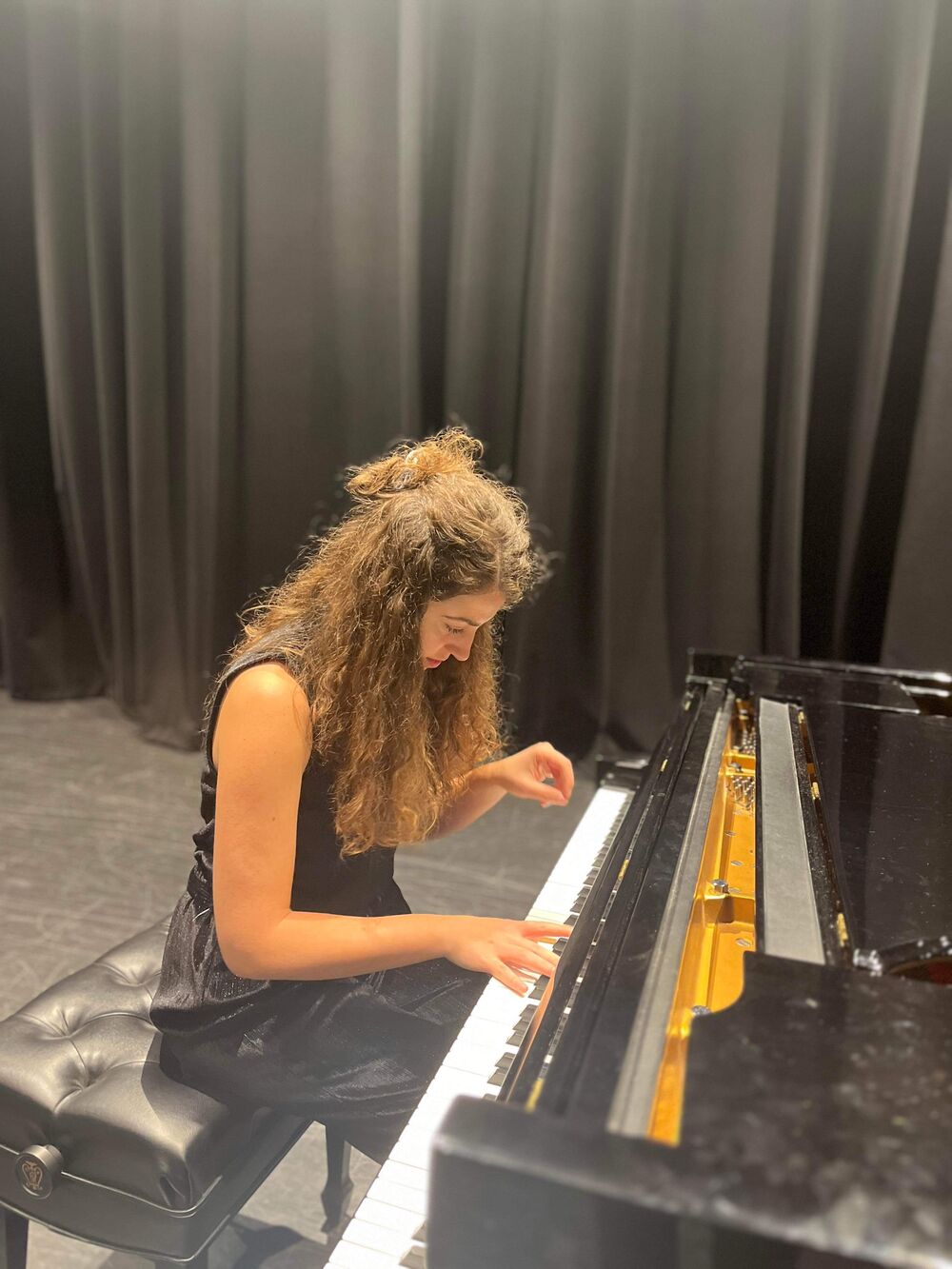 Playing at the piano before a dark stage curtain