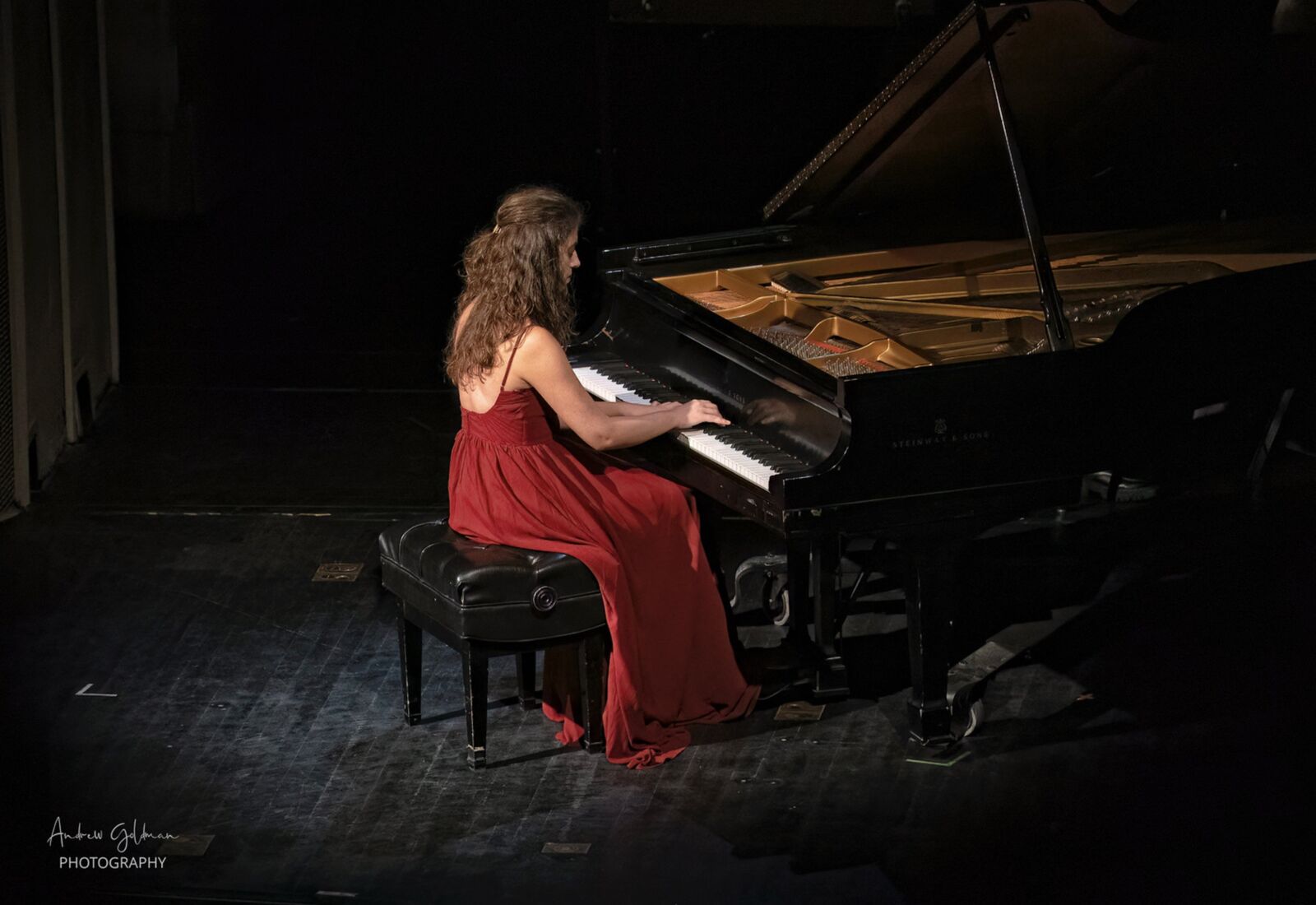 Playing a Steinway grand on a darkened stage in a red gown