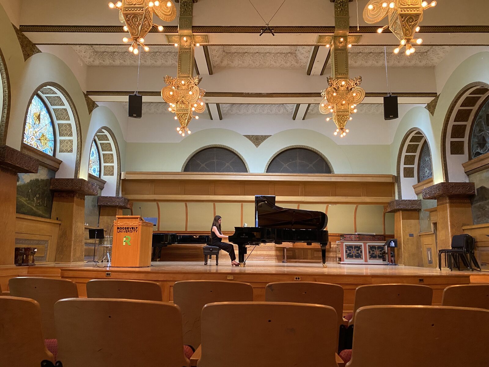 Performing at a grand piano in an ornate concert hall with chandeliers